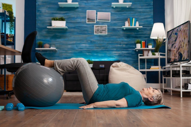 Senior woman performing a leg exercise with a stability ball during home physiotherapy